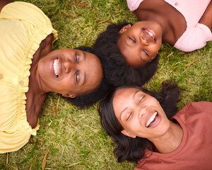 Looking Down On Three Generation Female Family With Eyes Closed Laughing And Lying On Grass Outdoors