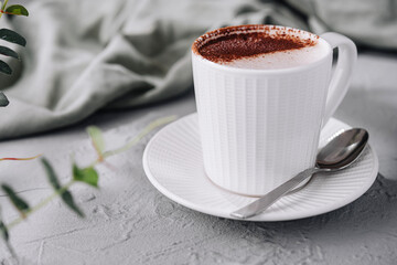 Fresh cappuccino in a white cup on a gray surface