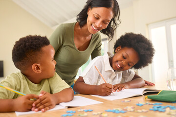 Family Indoors At Home With Mother Helping Children With Homework Sitting At Table