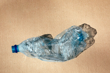 Crumpled empty transparent plastic bottle from water on a brown cardboard background. A planet...
