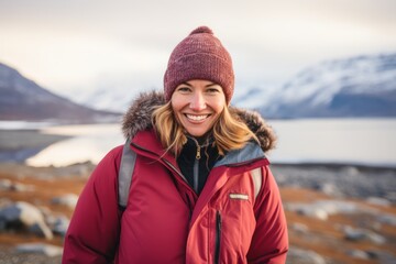 Portrait of a smiling woman in her 40s sporting a stylish varsity jacket in front of backdrop of an arctic landscape