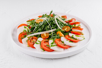 Fresh caprese salad with arugula on white plate