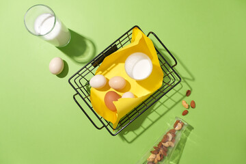 Top view of cooking concept on pastel green background. Flat lay with eggs and a cup of milk on basket. Layout for baking recipe, culinary, cooking blog