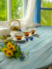 A serene setting of a morning tea session. Two cups of freshly brewed tea, accompanied by a white teapot, rest on a wooden table adorned with a blue cloth. Concept with copy space - 787042056