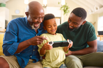 Grandfather With Father And Grandson Playing With Handheld Gaming Device At Home With Family