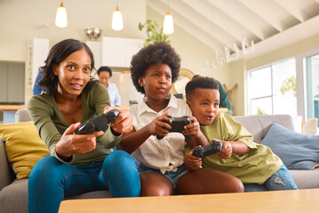 Excited Mother And Children Sitting On Sofa At Home Playing Computer Game 