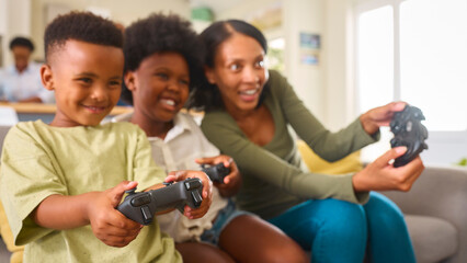 Excited Mother And Children Sitting On Sofa At Home Playing Computer Game 