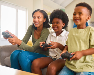 Excited Mother And Children Sitting On Sofa At Home Playing Computer Game 
