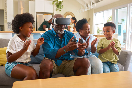 Grandparents With Grandchildren Wearing Virtual Reality Headset Playing Game At Home Together - Powered by Adobe