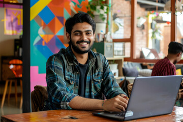 An optimistic Indian man works on his laptop in a vibrant office setting, expressing success and positivity in his endeavors.