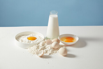 Minimalist layout about cooking on blue background including milk, egg and flour in center of...