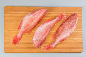 Frozen redfish with hoarfrost on cutting board on gray surface