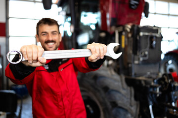 Happy caucasian serviceman holding wrench tool ready to repair tractor for agribusiness.
