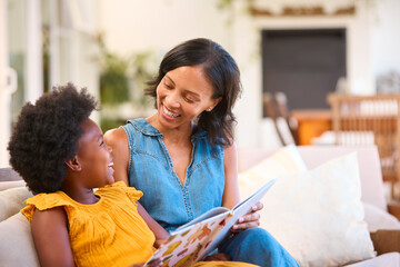 Family With Mother And Daughter Sitting On Sofa At Home Reading Book Together