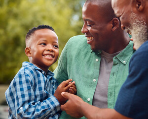 Three Generation Male Family Laughing Hugging Grandson Standing Outdoors In Countryside