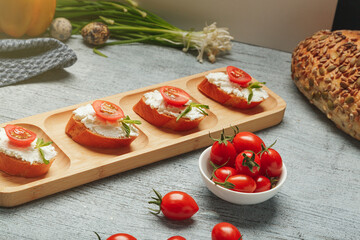 Healthy snack prepared from fresh baguette and cream cheese with tomato and greenery. Lunchtime recipe to cook at home