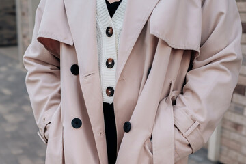 Street style fancy details of a knitted white button-up sweater and beige women's trench coat....