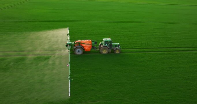Aerial view of farming tractor spraying on field with sprayer, herbicides and pesticides at sunset. Farm machinery spraying insecticide to the green field, agricultural natural seasonal spring works