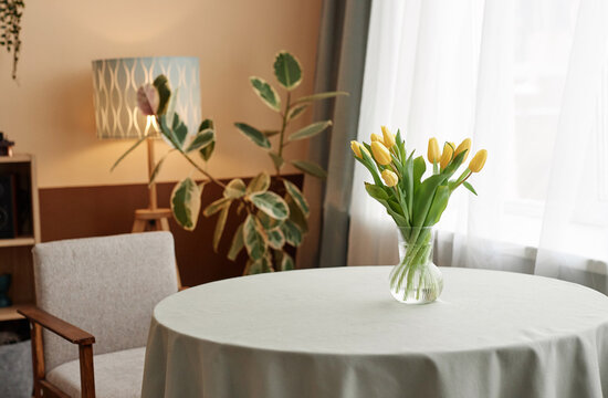 Background image of cozy room interior with yellow tulips bouquet on round dinner table copy space