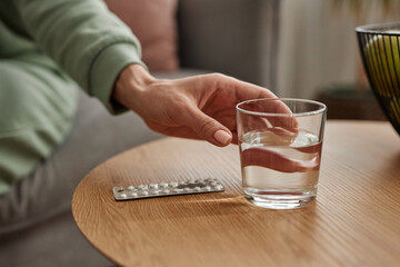 Close up of female hand reaching for glass of water with woman taking medicine at home copy space