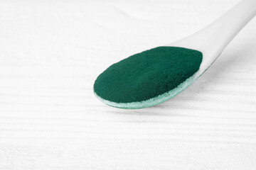 Green chlorella and spirulina powder in ceramic spoon, from above view, selective focus