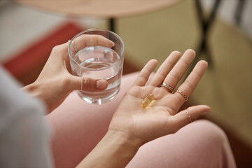 Top view closeup of unrecognizable woman taking vitamins at home and holding jelly pill in open hand copy space