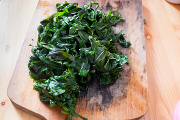 Boiled cassava leaves, on a wooden cutting board