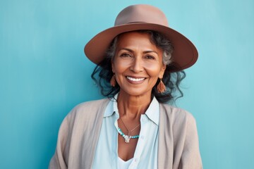 Portrait of a smiling indian woman in her 60s donning a classic fedora over pastel teal background - obrazy, fototapety, plakaty