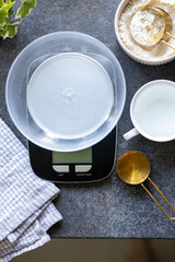 Scales, measuring spoon, napkin, water and flour on concrete kitchen counter. Concept of cooking, weighing ingredients for baking, making and feeding sourdough starter at home. Top view