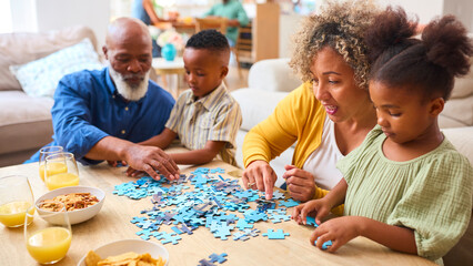 Grandparents With Grandchildren Indoors At Home Doing Jigsaw Puzzle With Parents In Background