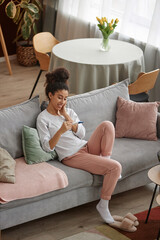 Vertical wide angle view at happy young woman holding pregnancy test sitting on couch in cozy home