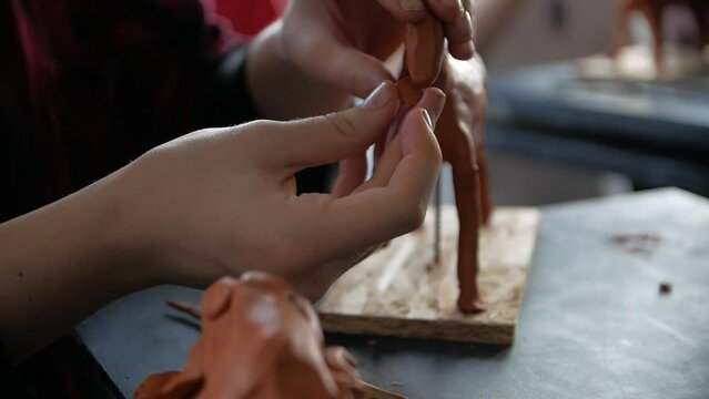 Close-up of child's hands sculping a horse from modeling clay in a workshop.