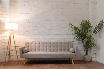 Interior mock up photo. White brick wall with leather sofa and pot with plant and light. Background photo with copy space for text. High quality photo