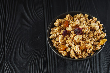 tasty crunchy granola with dried fruits on a black wooden rustic background
