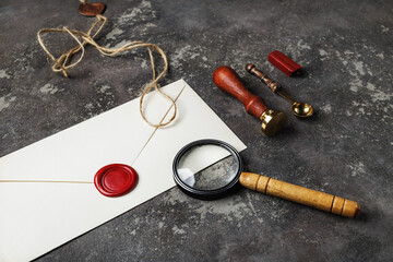 Blank retro stationery. Vintage envelope with wax seal, stamp, magnifier, spoon and rope on concrete background.