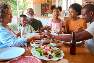 Multi-Generation Family Saying Prayer Before Eating Meal At Home Together