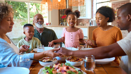 Multi-Generation Family Saying Prayer Before Eating Meal At Home Together