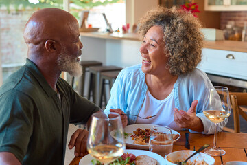 Smiling Senior Couple Enjoying Meal At Home Together And Drinking Glasses  Of Wine