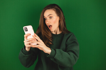Photo of pretty funny excited brunette woman open mouth hold telephone post youth blog read comments wear green pullover isolated green color background. Shock surprised woman.