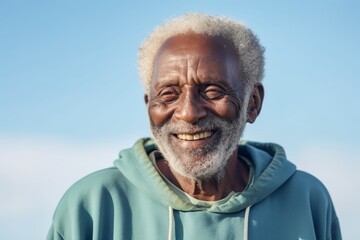 Portrait of a grinning afro-american elderly 100 years old man sporting a comfortable hoodie in soft blue background