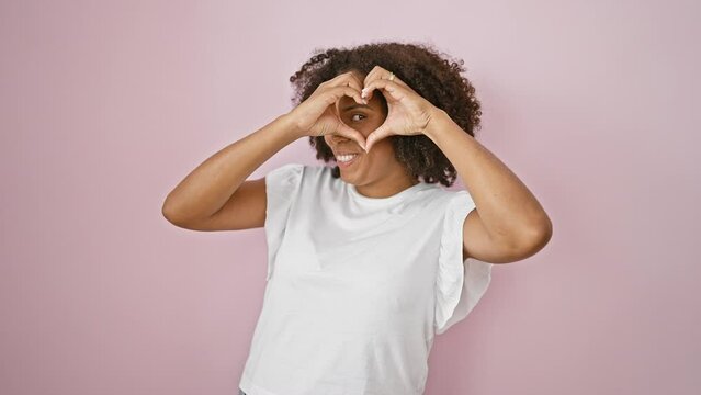 African american woman making heart shape with hands on pink background