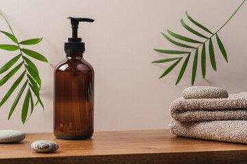 Brown recycled glass bottle with soap dispenser and stack of terry towels on wooden shelf. Caddy...