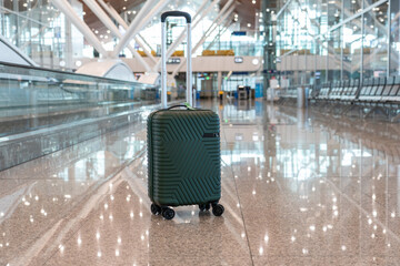 Green stylish suitcase against sparkling light empty blurred airport background. Concept of business travel, summer vacation, adventure