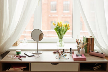 Front view background image of makeup and personal items on table by window with tulips bouquet copy space