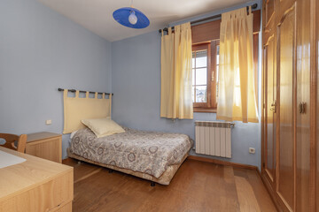 Classic bedroom with a single bed covered with a flower-print bedspread, a wooden window with curtains and light blue painted walls