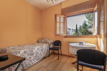 Classic bedroom with single bed covered with flower-printed bedspread, wooden window with views and peach-painted walls