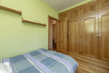 Classic bedroom with a bed covered with a striped bedspread, a large built-in wardrobe with oak...