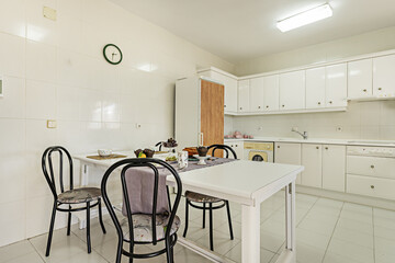 Large breakfast table with food on it in a kitchen with white lacquered furniture and integrated appliances