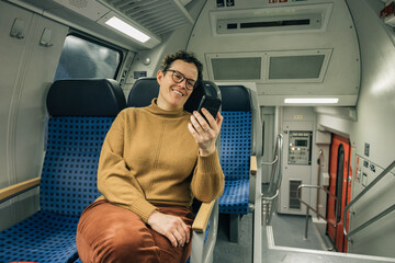 Woman smiling while looking at the smart phone while traveling by train