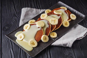 fresh tasty pancakes with banana and condensed milk on a black rustic background